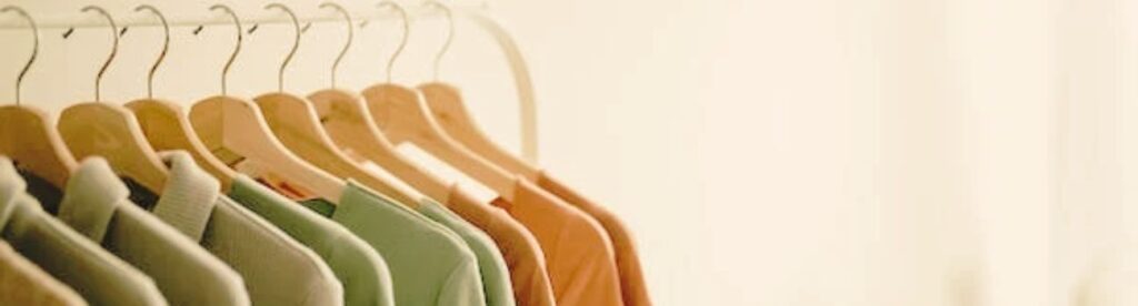 Varias camisetas colgadas en perchas de madera y perfectamente ordenadas por colores en tonos tierra.