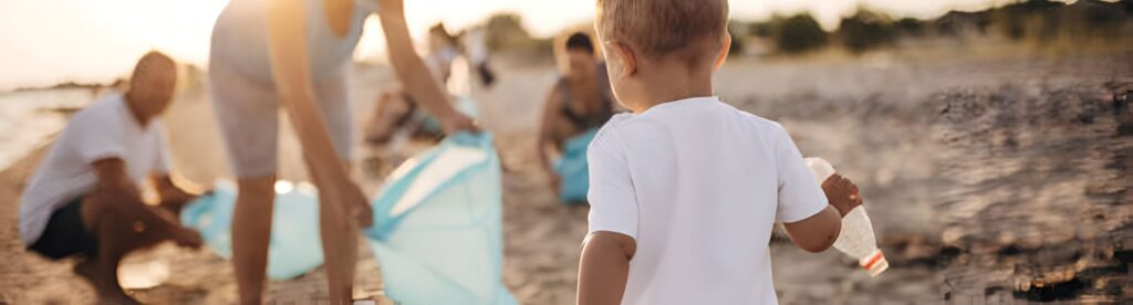 Familia en la playa recogiendo basura de plástico siendo ayudada por su bebé que también recoge a modo de juego.