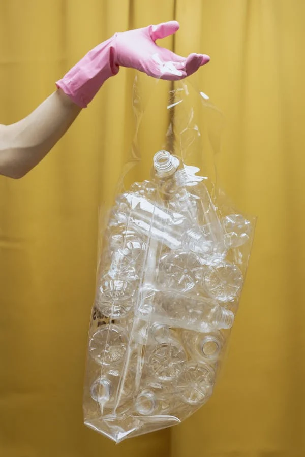 Mano aguantando una bolsa llena de envases de plástico en un fondo amarillo.