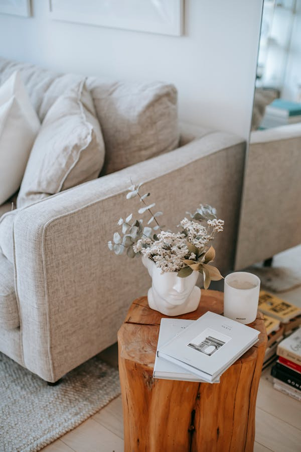 Foto parcial de un sofá en tonos beige al lado de una mesita con un jarrón de flores, una vela y un libro. Todo acogedoramente dispuesto.