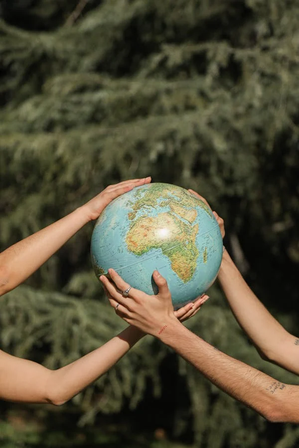 Fondo de vegetación sobre el cual dos personas están sujetando una maqueta del globo terrestre 