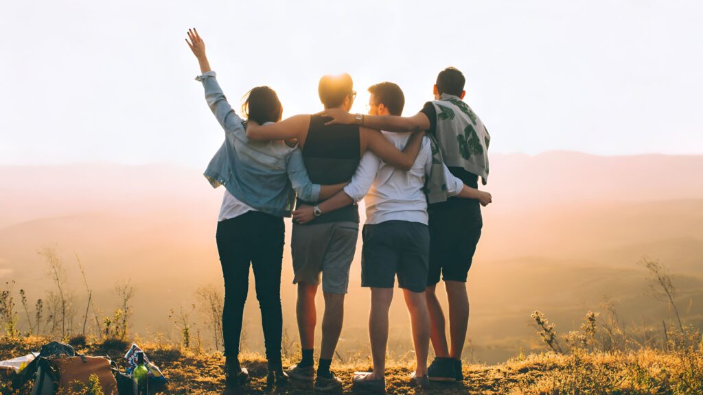 Cuatro personas adultas vistas de espaldas, admirando un paisaje delante de su horizonte y vitoreándolo. La sostenibilidad es clave para el bienestar colectivo.