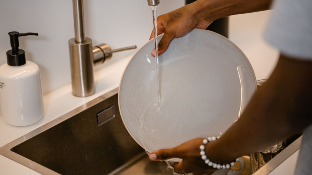 Persona lavando un plato bajo el agua de un grifo.