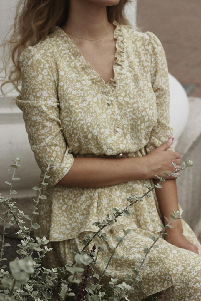 Mujer con un vestido estampado con flores pequeñas sentada entre flores blancas.