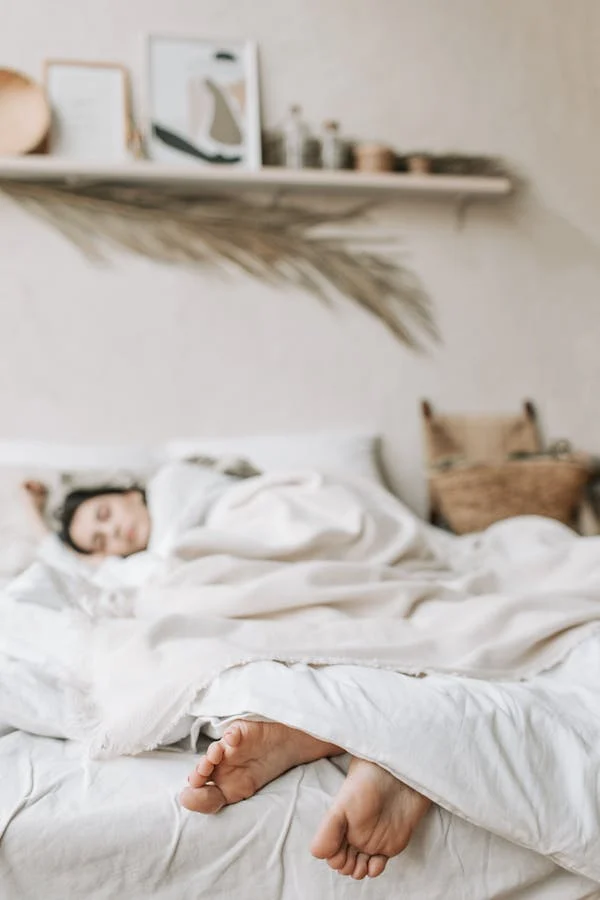 Mujer durmiendo entre sábanas blancas. El foco del objetivo son sus pies, mientras su rostro queda ligeramente desenfocado al estar más alejado de la cámara.