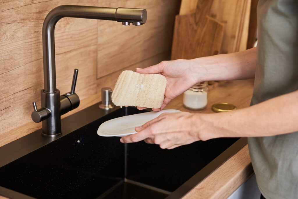 Mujer lavando platos con esponja de lufa natural, orgánica y eco-friendly. Concepto de residuo cero.